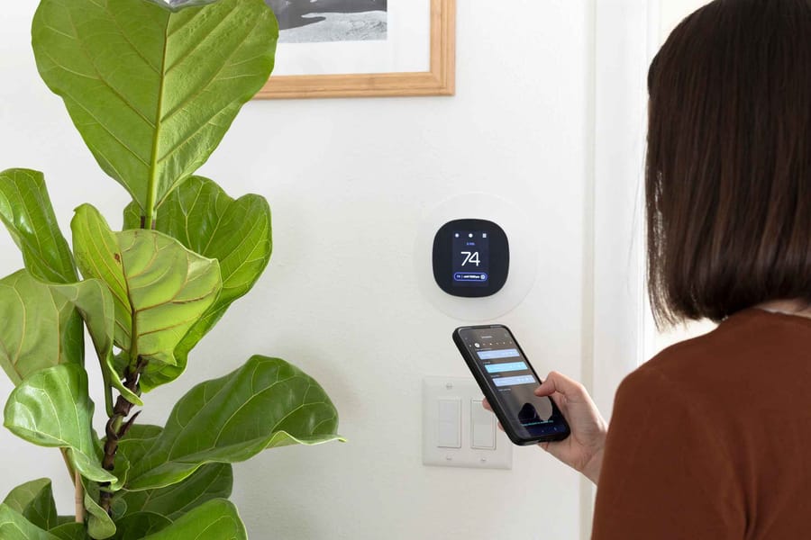 A woman using her phone to program a smart thermostat